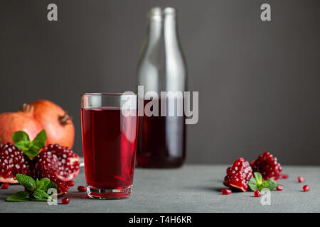 Auf grauem Beton Hintergrund ist eine Flasche Glas mit Granatapfelsaft. In der Nähe befinden sich mehrere Schichten von Granatäpfeln. Stockfoto