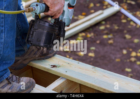 Bau eines neuen oberirdischen Deck, Tischler Installieren eines Holzboden Terrasse im neuen Haus ein Mann mit Pneumatic nailer Gun Stockfoto