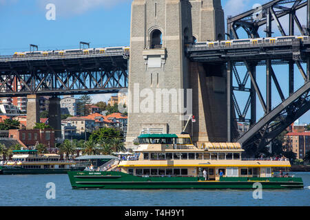 Die Fähre von Sydney mit dem Namen MV May Gibbs fährt am Hafen von Sydney vorbei an der hafenbrücke von sydney, Sydney, Australien, wobei der Zug von Sydney die Hafenbrücke überquert Stockfoto