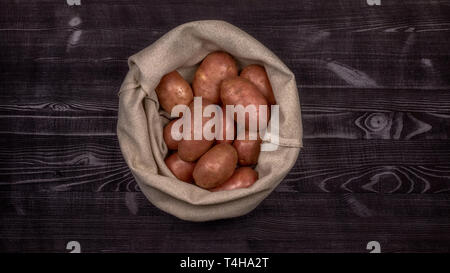Red rohe Kartoffeln in einer Tasche auf einem schwarzen rustikalen Holztisch Hintergrund für Reinigung und Schneiden beim Kochen ein gebraten, geschmort oder gekocht Essen vorbereitet Stockfoto