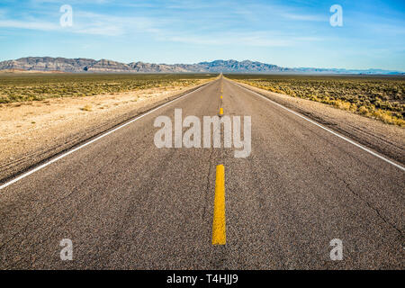 Gepunktete gelbe Linie in der langen, geraden Autobahn durch die Wüste von Nevada. Die Extraterrestrail Highway in der Nähe von Area 51 ist wüst und öde. Stockfoto