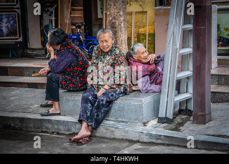 Eine Gruppe von drei glückliche ältere chinesische Frauen sitzen und entspannen in der Seitenstraße. Im gemeinsamen Leben in China. Asiatische ältere Frauen. Friedliche Nachbarschaft. Stockfoto