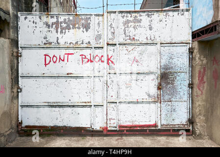 Weißes altes rostiges Metall Eingangstor, geschlossen und verriegelt und mit Stacheldraht gesichert. 'Don't Block' auf dem Tor geschrieben wird. Stockfoto