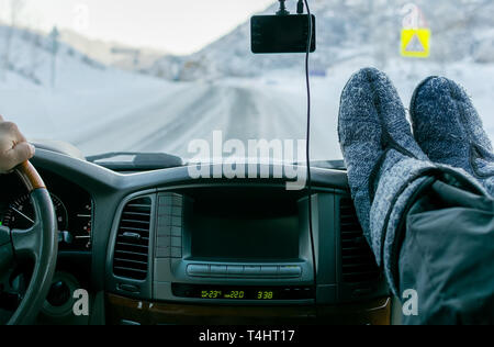 Blick auf das Auto panel mit Monitor, Bedientasten, die Hände am Lenkrad und den Beifahrersitz Füße im warmen Stiefel und Anzeigen der Winter r Stockfoto