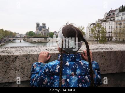 Paris, Frankreich. 16 Apr, 2019. Ein Mädchen Uhren die Kathedrale Notre Dame nach einem Brand in Paris, Frankreich, am 16. April 2019. Der französische Präsident Emmanuel längestrich am Dienstag gelobte Kathedrale Notre Dame, die durch einen Brand am Montag abend verwüstet, innerhalb von fünf Jahren wieder aufzubauen, in der die französische United zu bleiben. In der frühen Montag Abend, brach ein Feuer in der berühmten Kathedrale. Online footage zeigte dicker Rauch Wogenden von oben auf den Dom und die riesige Flammen zwischen seinen zwei Glockentürme engulfing der Turm und das gesamte Dach, die beide später zusammenbrach. Stockfoto