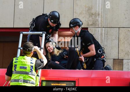 London, Großbritannien. 17 Apr, 2019. Polizisten ein Demonstrant, der sich in einem Gurt in Canary Wharf Station in London auf dem Dach eines DLR-Zug Wagen geklebt, Großbritannien am 17. April 2019. Dies ist Teil eines fortschreitenden Klimawandel Proteste in London. Credit: Claire Dohert/Alamy leben Nachrichten Stockfoto