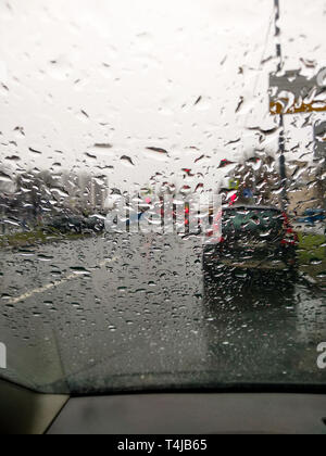 Regentropfen auf der Windschutzscheibe. Blick aus dem Auto. Rote Ampel. Stadtbild. Stockfoto