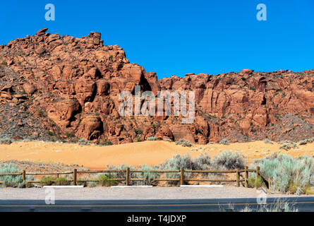 Anmelden Zaun mit Salbei Pinsel gibt Weg für gelbe Wüste Sand Dünen mit karge raue Red Rock Mountain unter einem strahlend blauen Himmel. Stockfoto