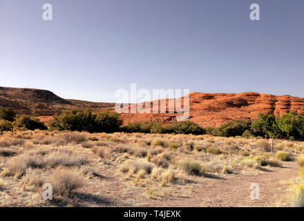 Schmutz Wanderweg führt durch Sagebrush in Richtung grüne Bäume und steile Rote felsigen Hügeln unter einem hellen Blau Lila Himmel. Stockfoto