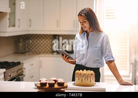 Frau, die in der Küche Verwendung digitaler Tablet mit Gebäck auf der Arbeitsplatte in der Küche. Köchin an Ihrem Tablet-PC in der Küche. Stockfoto