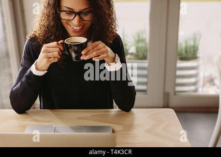 Lächelnde Frau im Cafe Kaffee trinken saßen und am Laptop auf dem Tisch. Glückliche junge Frau in einem Cafe. Stockfoto