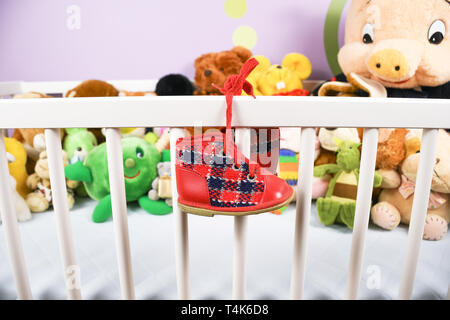 Gruppe von farbigen flauschigen Stoff Spielzeug closeup mit hängenden roten kleinen Baby Schuh auf einem weißen Krippe Zaun Stockfoto