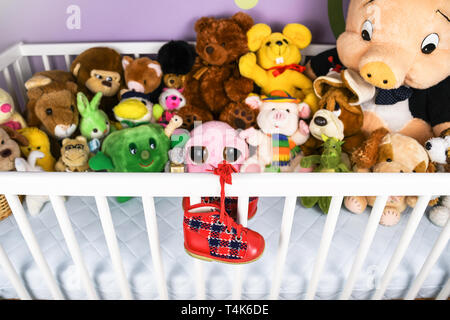 Gruppe von farbigen flauschigen Stoff Spielzeug closeup mit hängenden roten kleinen Baby Schuh auf einem weißen Krippe Zaun Stockfoto