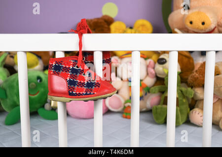 Gruppe von farbigen flauschigen Stoff Spielzeug closeup mit hängenden roten kleinen Baby Schuh auf einem weißen Krippe Zaun Stockfoto