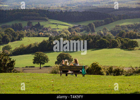 Zwei Frauen, die Freunde sitzen und plaudern auf einer Bank in der Sonne mit Blick auf die schöne Landschaft der Surrey Hills von Newlands Ecke Stockfoto