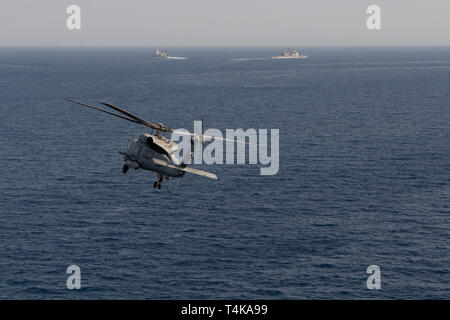 Einem MH-60R Sea Hawk, Hubschrauber Maritime Strike Squadron (HSM) 71 zugewiesen, fliegen wie die Royal Danish Navy Fregatte HDMS Niels Juel (F 363), links, und der geführten-missile Cruiser USS Mobile Bay (CG53) brechen Weg von einer Bildung im Roten Meer, 15. April 2019. Die John C Stennis Carrier Strike Group ist in die USA 5 Flotte Bereich der Maßnahmen zur Unterstützung der Marine im Einsatz für die Stabilität und Sicherheit in der Region zu gewährleisten und verbindet das Mittelmeer und den Pazifischen Raum durch den westlichen Indischen Ozean und drei strategischen Punkten ersticken. (U.S. Marine Foto von Masse Communicati Stockfoto