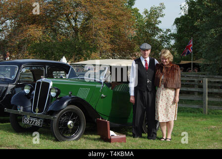 Der Mann und die Frau in der 40er Jahre Kostüm, um einen Oldtimer Sportwagen mit einem offenen Picknickkorb, Stoke Bruerne, Northamptonshire, Großbritannien Stockfoto