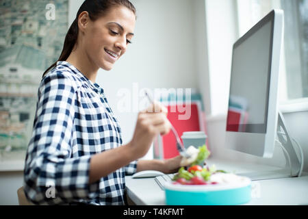 Mitarbeiterin im Büro in gesunden Chicken Salat Mittagessen am Schreibtisch Stockfoto