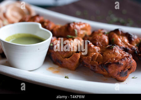 Chicken Tikka Kebabs serviert mit würzigen Pudina/Mint Chutney/Dip und cremig Zwiebeln. Stockfoto