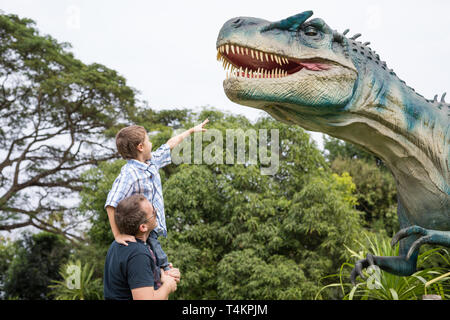Gerne Vater und Sohn spielen in das Abenteuer Dino Park am Tag Zeit. Menschen, die Spaß im Freien. Konzept der Sommerferien und freundliche Familie. Stockfoto