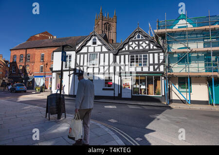 Ein älterer Mann, der einen Shopping Bag Spaziergänge in den Schatten in der King Street, Ludlow, Shropshire, Großbritannien Stockfoto