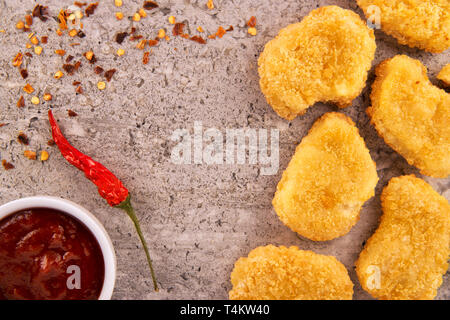 Chicken Nuggets mit einem Red Hot Chili Pepper und eine Schale mit Soße auf einer konkreten Textur Hintergrund. Direkt oberhalb. Stockfoto