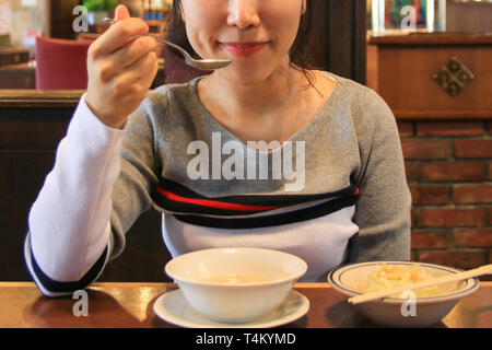 Aisan (Koreanisch) junge hübsche Frau essen Suppe mit Löffel Stockfoto