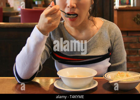 Aisan (Koreanisch) junge hübsche Frau essen Suppe mit Löffel Stockfoto