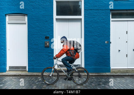 Ein Mann auf einem Fahrrad radfahren Vergangenheit ein Haus bemalt blau und weiß. Stockfoto