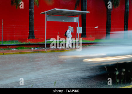 Person steht im Regen an der Haltestelle, während ein Auto fährt an Ihm vorbei Stockfoto
