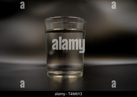 Nur ein Glas Wasser auf einem dunklen Holztisch. Mineralwasser in einem Glas auf einem schwarzen Hintergrund. Ein Glas mit Wasser Stockfoto