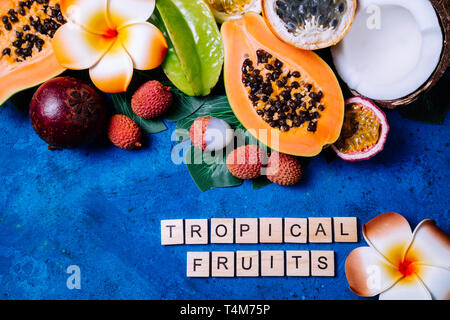 Sommer tropischen Hintergrund mit exotischen verschiedene Früchte, grünen Palmen Blätter und Blumen auf blau. Obst Hintergrund. Ansicht von oben Stockfoto