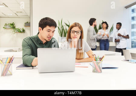 Junge Kollegen arbeiten zusammen auf Laptop Computer in Coworking Büro Stockfoto