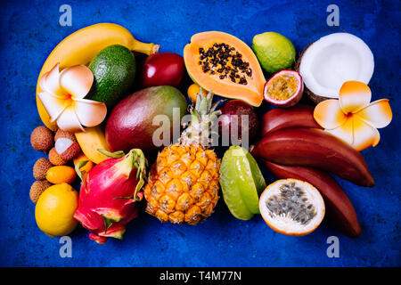 Sommer tropischen Hintergrund mit exotischen verschiedene Früchte, grünen Palmen Blätter und Blumen auf blau. Obst Hintergrund. Ansicht von oben Stockfoto