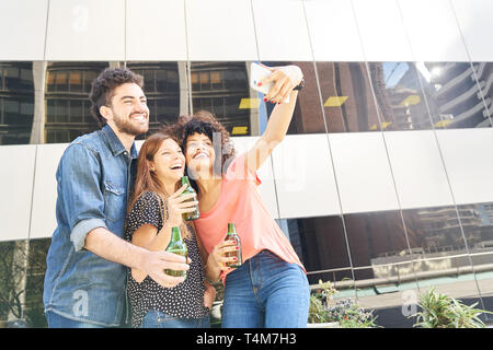 Drei fröhlicher junger Leute vor einem Bürogebäude, trinken Bier und ein Foto von selfie Stockfoto