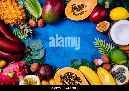 Sommer tropischen Hintergrund mit verschiedenen exotischen Früchten und grünen Palmen Blätter auf Blau. Obst Hintergrund. Ansicht von oben, kopieren Raum Stockfoto