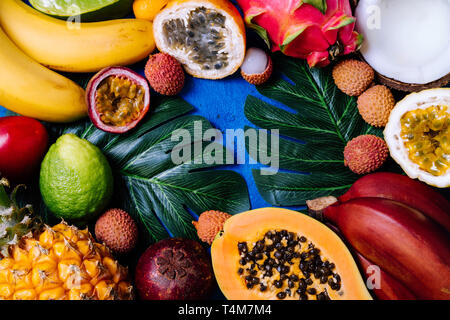 Sommer tropischen Hintergrund mit verschiedenen exotischen Früchten und grünen Palmen Blätter auf Blau. Obst Hintergrund. Ansicht von oben, kopieren Raum Stockfoto
