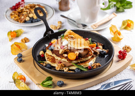 Köstlich süßen amerikanische Pfannkuchen serviert auf einem Bratpfanne mit frischem Obst, Nüsse und Schokolade Sauce Stockfoto