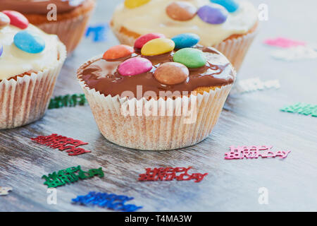 Selbstgemachte Muffins, beschichtet mit Schokolade und schokolade Linsen auf Holz- Oberfläche neben kleinen Geburtstag Dekoration mit den Worten: Alles Gute zum Geburtstag Stockfoto