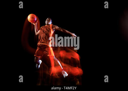 Höher als die Wolken. Afrikanisch-amerikanischen Jungen Basketballspieler der roten Team in Aktion und Neonlicht über dunklen Studio Hintergrund. Konzept für Sport, Bewegung, Energie und Dynamik, gesunde Lebensweise. Stockfoto