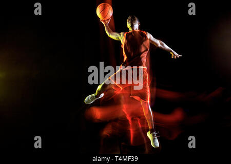 Unaufhaltsam. Afrikanisch-amerikanischen Jungen Basketballspieler der roten Team in Aktion und Neonlicht über dunklen Studio Hintergrund. Konzept für Sport, Bewegung, Energie und Dynamik, gesunde Lebensweise. Stockfoto