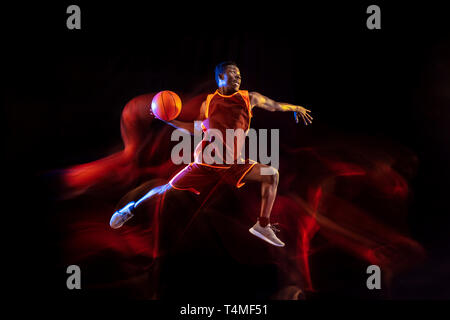 Siehe das Ziel. Afrikanisch-amerikanischen Jungen Basketballspieler der roten Team in Aktion und Neonlicht über dunklen Studio Hintergrund. Konzept für Sport, Bewegung, Energie und Dynamik, gesunde Lebensweise. Stockfoto