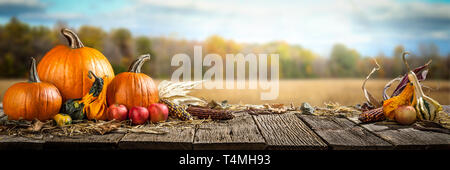 Thanksgiving mit Kürbisse, Äpfel und Maiskolben auf Holztisch mit Feld Bäume und Himmel im Hintergrund Stockfoto