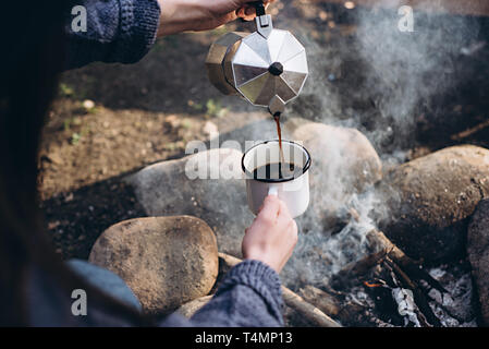 Nahaufnahme des Traveler's Hand gießt sich heißen Getränk in den Bergen in der Nähe von Feuer. Ein junger Tourist Frau Getränke bei einem heißen Getränk aus einer Tasse und Genießen Stockfoto