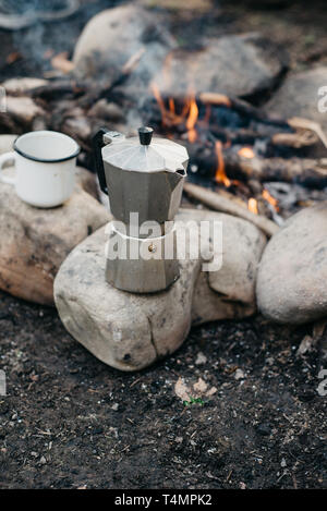 Nahaufnahme der weißen Schale und Kaffeemaschine in der Nähe von Feuer. Konzept Abenteuer aktiv Urlaub im Freien. Sommer Camp Stockfoto