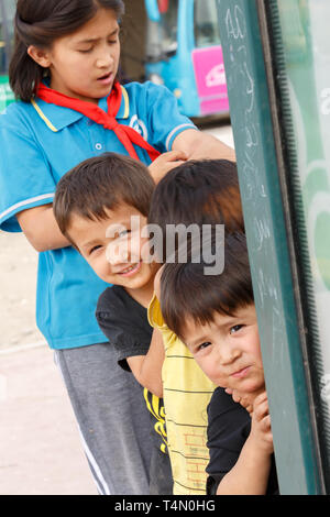 KASHGAR, XINJIANG/CHINA - Oktober 1, 2017: Uigurischen Kinder neugierig peeking an der ausländischen Fotografen. An einer Bushaltestelle in Kashgar gefangen. Stockfoto