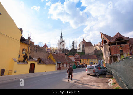 Alba Iulia, Rumänien - 9. April 2019: Alter Mann mit einem Stock zu Fuß auf der Straße in Sighisoara. Bunte Häuser, der Glockenturm und die Kirche der D Stockfoto