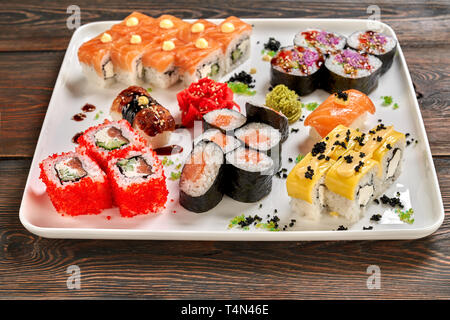 Verschiedene Arten von Nigiri, Maki und Uramaki. Philadelphia, Käse uramaki, veggie Brötchen und Nigiri mit Wasabi und eingelegtem Ingwer auf weiße Platte, Holz- Hintergrund. Stockfoto