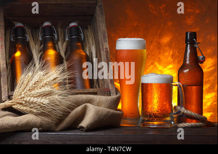 Biergläser mit Holzkiste voller Bierflaschen und Weizenähren auf Tisch Stockfoto