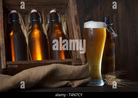 Bier Glas mit Holzkiste voller Bierflaschen und Weizenähren Stockfoto